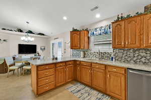 Kitchen with light stone countertops, brown cabinetry, stainless steel dishwasher, a peninsula, and vaulted ceiling