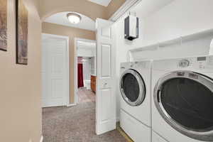 Laundry area with arched walkways, light colored carpet, water heater, and separate washer and dryer
