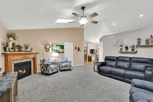 Living area with vaulted ceiling, carpet floors, a ceiling fan, and a fireplace