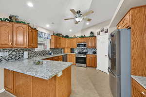 Kitchen with stainless steel appliances, backsplash, lofted ceiling, a peninsula, and light stone countertops