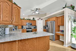 Kitchen with brown cabinets, backsplash, appliances with stainless steel finishes, a peninsula, and lofted ceiling