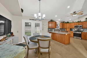 Kitchen featuring appliances with stainless steel finishes, brown cabinetry, backsplash, decorative light fixtures, and light stone counters