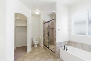 Contemporary bathroom featuring a white soaking tub with dark bronze fixtures, a tiled shower with a glass enclosure, and a frosted window