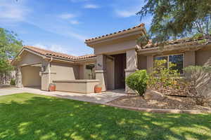 Stucco exterior residence featuring a tile roof, an attached garage, a structured stone façade accent, and a manicured lawn