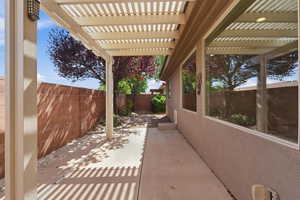 Covered patio featuring a slatted pergola, concrete flooring, and an exterior stucco finish