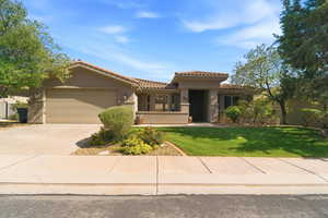 Stucco exterior with a tile roof, featuring an integrated two-car garage, a covered entry, a grass lawn, and mature landscaping