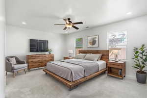 Spacious room featuring light-colored carpeting, multiple windows for natural illumination, a ceiling fan with integrated lighting, and recessed ceiling lights