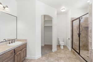 Bathroom featuring an expansive tiled shower with a black-framed glass enclosure, a vanity with wood-finish cabinetry, a single basin sink, and a large mirror