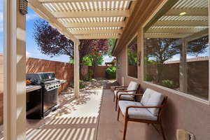 Covered patio area featuring a slatted pergola, concrete flooring, exterior wall with multiple windows, and block wall perimeter