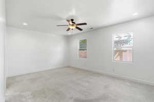 Spacious room featuring light-toned carpeting, two windows, recessed lighting, a ceiling fan with integrated lighting, and white baseboards