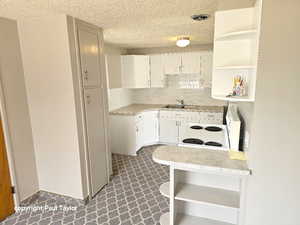 Kitchen featuring open shelves, light countertops, electric range, white cabinetry, and a textured ceiling