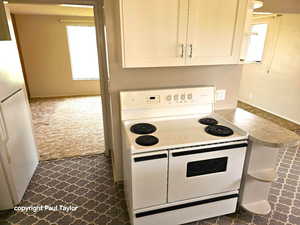 Kitchen with white appliances, white cabinetry, dark colored carpet, and light countertops