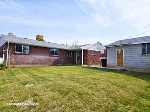 Rear view of house featuring a lawn, a chimney, and brick siding