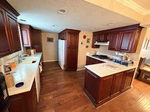 Kitchen with a peninsula, light countertops, dark wood-type flooring, white appliances, and a textured ceiling