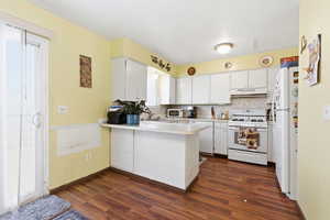 Kitchen featuring a peninsula, white cabinetry, white appliances, light countertops, and dark wood-type flooring