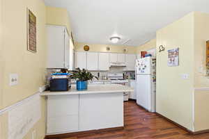 Kitchen featuring white cabinetry, a peninsula, light countertops, white appliances, and tasteful backsplash