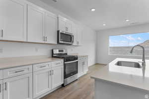 Kitchen featuring stainless steel appliances, white cabinetry, light wood finished floors, recessed lighting, and light stone counters