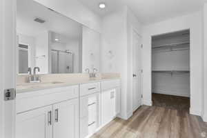Full bath featuring a walk in closet, a stall shower, double vanity, and light wood-style floors