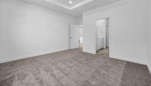 Unfurnished bedroom with ensuite bathroom, carpet floors, recessed lighting, and a tray ceiling