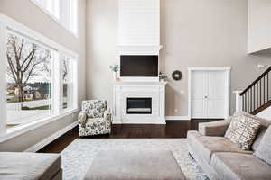 Living room featuring a towering ceiling, dark wood finished floors, a fireplace, and stairs