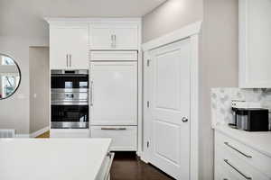 Kitchen featuring white cabinetry, paneled built in refrigerator, light stone counters, tasteful backsplash, and dark wood-style floors