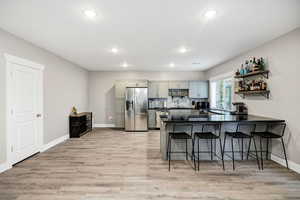 Kitchen featuring appliances with stainless steel finishes, gray cabinets, a kitchen breakfast bar, a peninsula, and light wood-style floors