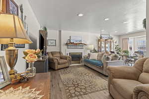 Living area with a glass covered fireplace, a textured ceiling, recessed lighting, and wood finished floors