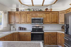 Kitchen featuring brown cabinetry, stainless steel appliances, tasteful backsplash, and tile counters