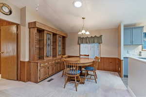 Dining space with wood walls, a wainscoted wall, light carpet, lofted ceiling, and a chandelier