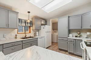 Kitchen with gray cabinetry, vaulted ceiling, white appliances, hanging light fixtures, and light wood-type flooring