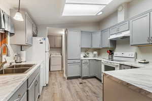 Kitchen featuring gray cabinets, white range with electric cooktop, washer / dryer, vaulted ceiling, and hanging light fixtures