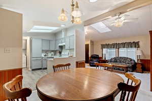 Dining room with a wainscoted wall, a skylight, wooden walls, vaulted ceiling, and a ceiling fan