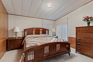 Bedroom featuring a textured ceiling, wood walls, lofted ceiling, carpet, and a wainscoted wall