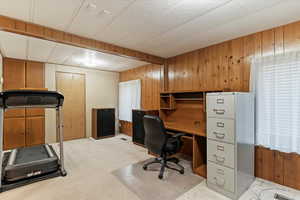 Office space featuring healthy amount of natural light, wooden walls, and light carpet