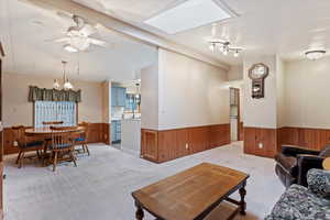 Living area with wood walls, light colored carpet, a wainscoted wall, ceiling fan, and a skylight