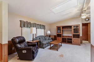 Living room featuring lofted ceiling, light colored carpet, a skylight, wooden walls, and a wainscoted wall