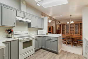 Kitchen featuring gray cabinets, white appliances, hanging light fixtures, under cabinet range hood, and vaulted ceiling
