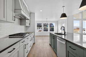 Kitchen with hanging light fixtures, gray cabinetry, stainless steel appliances, custom range hood, and decorative backsplash