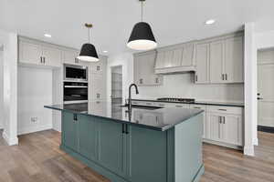 Kitchen with a center island with sink, custom range hood, stainless steel appliances, dark stone counters, and decorative backsplash