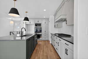 Kitchen with a kitchen island with sink, decorative light fixtures, dark stone counters, tasteful backsplash, and light wood-style floors
