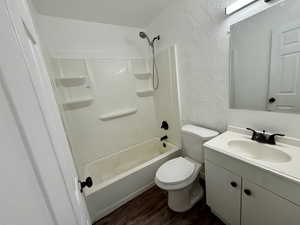 Full bathroom with a textured wall, vanity, dark wood finished floors, and washtub / shower combination