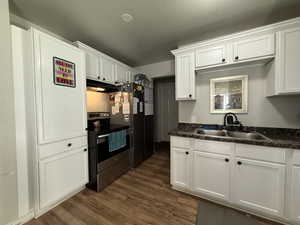 Kitchen featuring white cabinetry, stainless steel appliances, dark countertops, and dark wood-style flooring