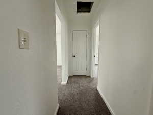Hallway with dark colored carpet and a textured wall
