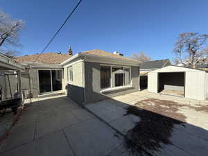 Rear view of property featuring a storage shed, brick siding, a shingled roof, and a patio area