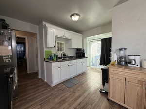 Kitchen with white cabinets, dark wood-type flooring, freestanding refrigerator, and dark countertops