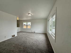 Unfurnished living room featuring dark colored carpet and baseboards