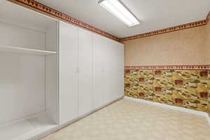 Interior space with light flooring, wallpapered walls, and a textured ceiling