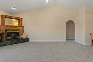 Unfurnished living room with vaulted ceiling, arched walkways, carpet flooring, a premium fireplace, and a ceiling fan