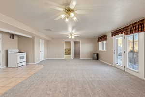 Unfurnished living room featuring a textured ceiling, light carpet, light tile patterned flooring, and ceiling fan