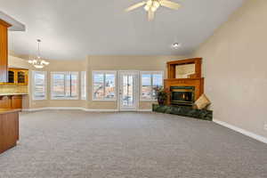 Unfurnished living room featuring lofted ceiling, a fireplace, a chandelier, light colored carpet, and ceiling fan